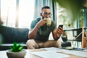 Man drinking coffee with phone and bills