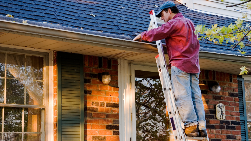 man cleaning out the gutters on a home