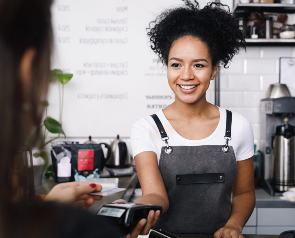 Smiling cashier accepting payment over nfc technology, looking on a buyer