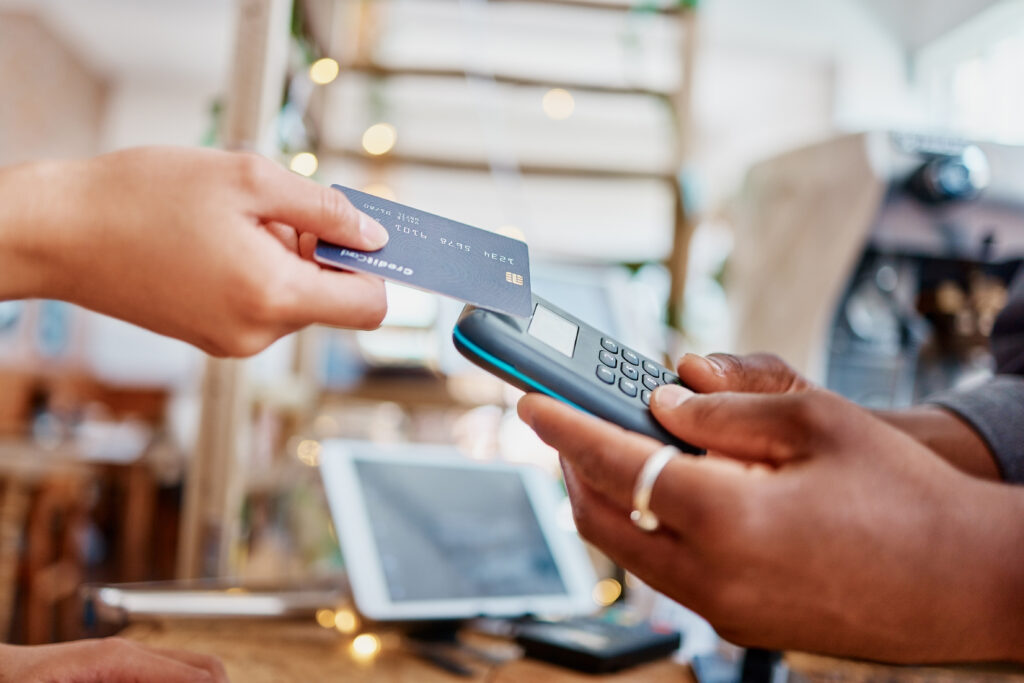 Closeup of unknown mixed race customer using a wireless credit card machine to pay for her coffee.