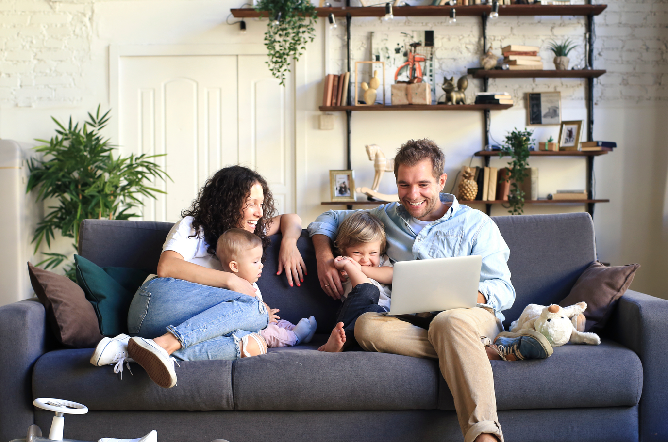 Family with two young children sitting on a couch with a laptop.
