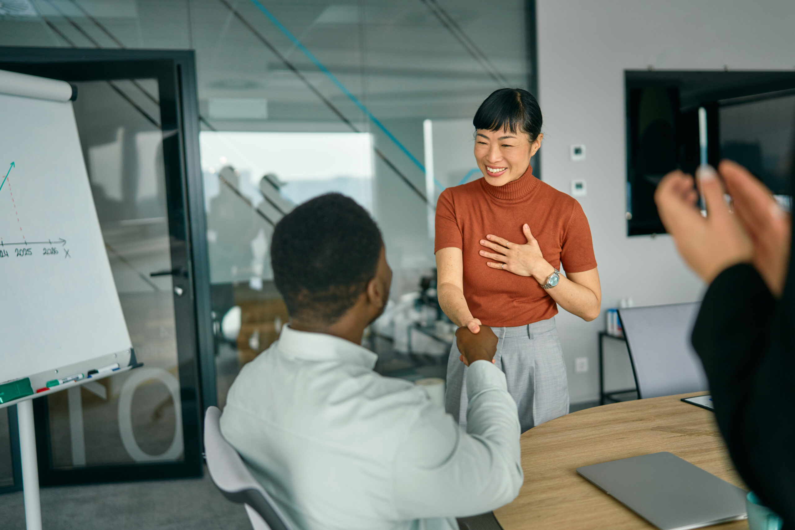 Business professionals shaking hands during a meeting in a modern office conference room.
