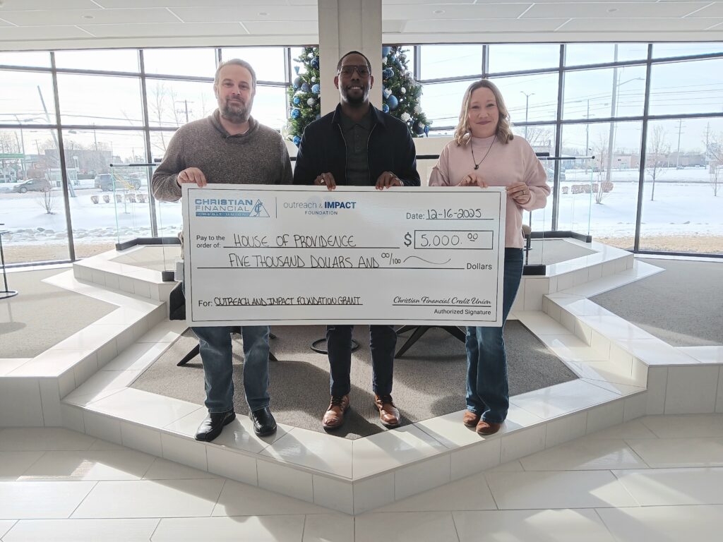 Three people standing in a bright lobby holding a ceremonial $5,000 grant check presented to House of Providence.