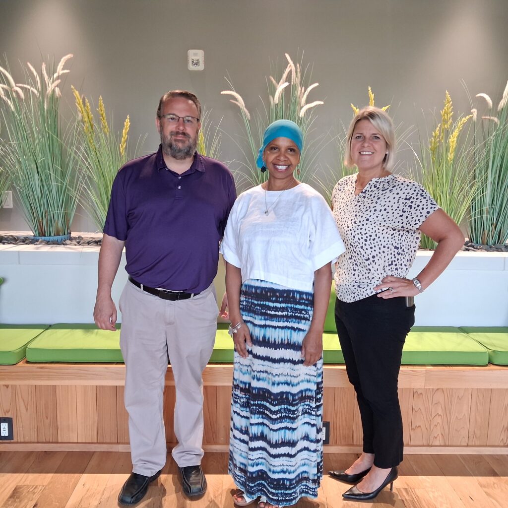 Three people stand for a picture with green plants behind them inside.