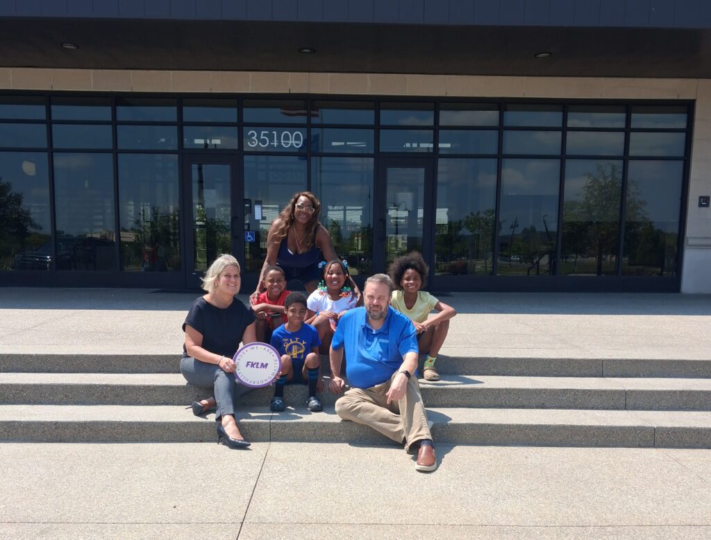 Participants sit and stand together outside a facility during a donation presentation.