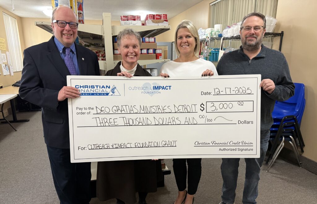 Four people standing indoors holding a ceremonial check for $3,000 presented to Deo Gratias Ministries Detroit.