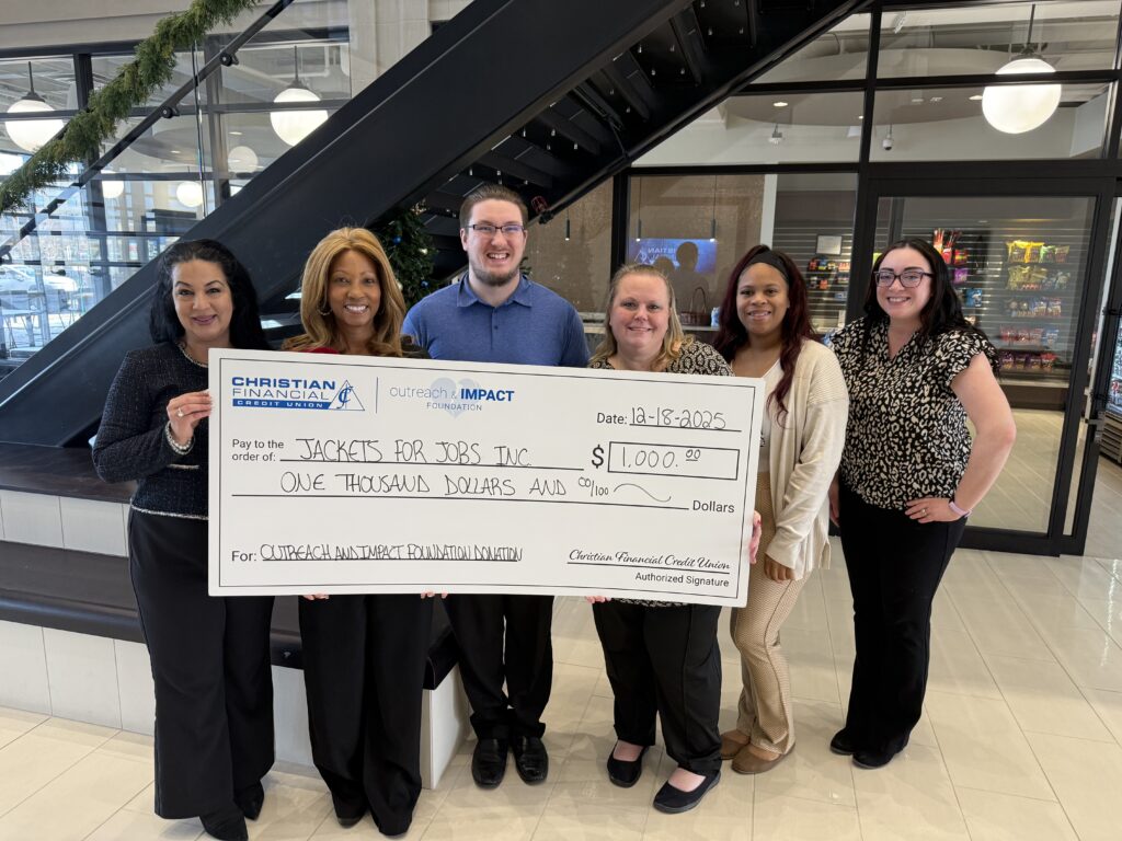 Six people hold a ceremonial $1,000 donation check for Jackets for Jobs during a presentation event.