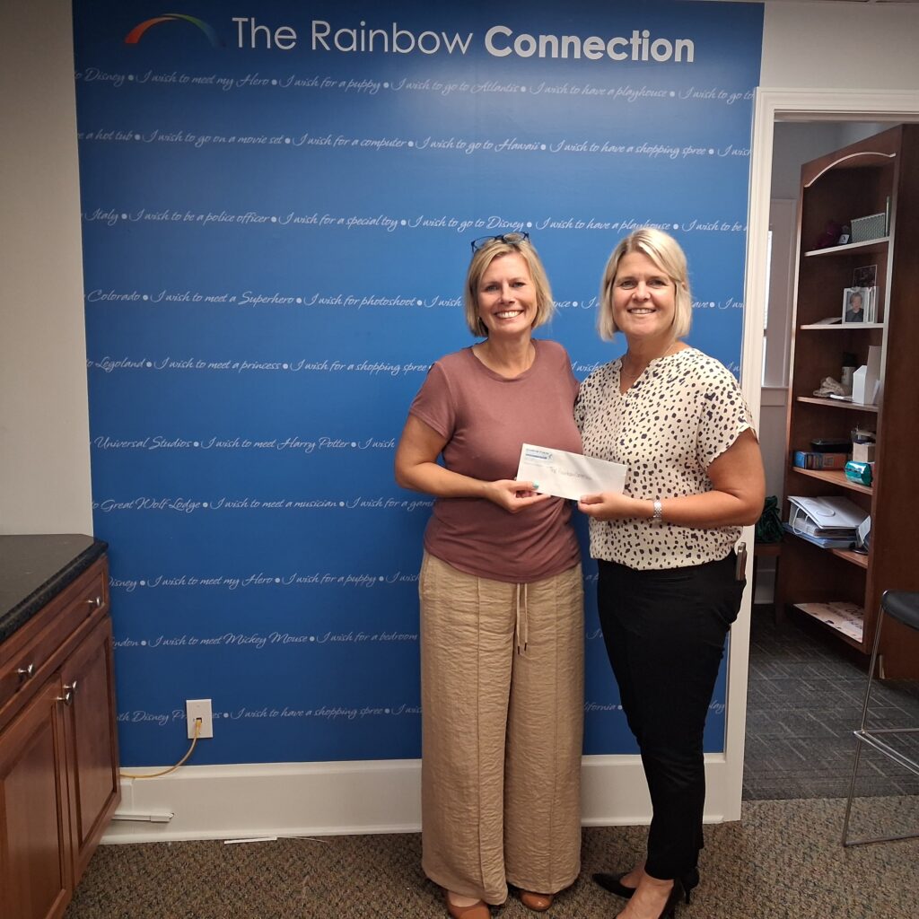 Two individuals stand together holding a ceremonial check in front of a blue wall.