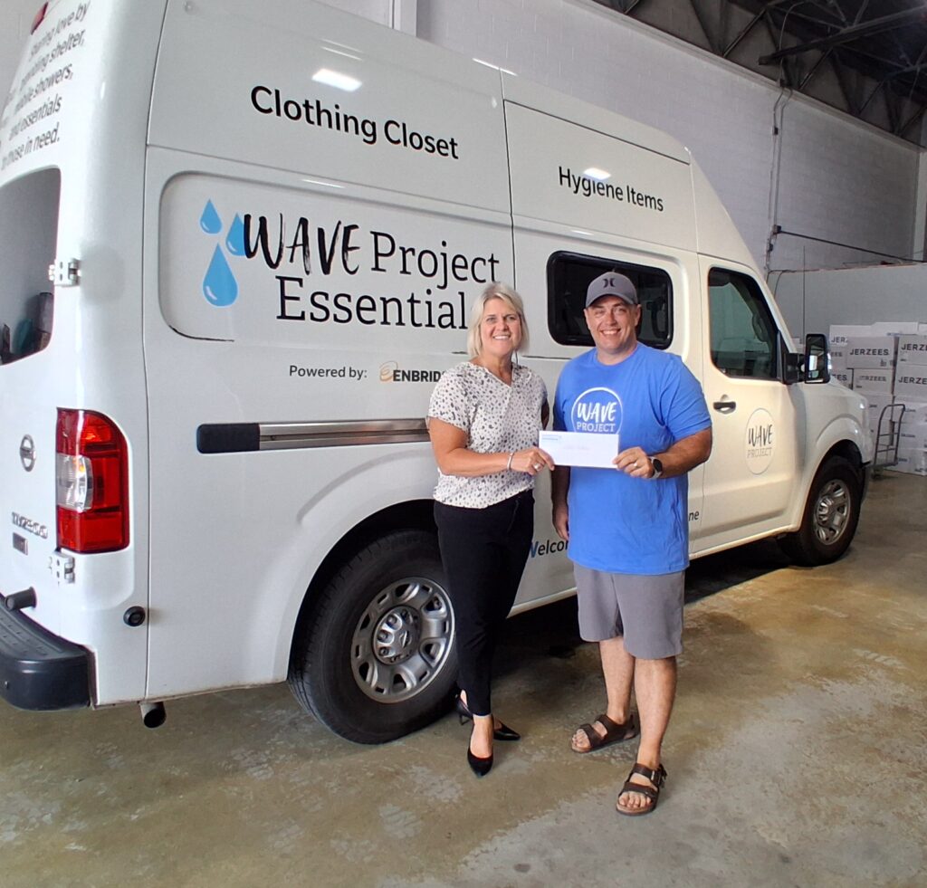 An individual poses with a ceremonial check near a branded van or mobile service vehicle.
